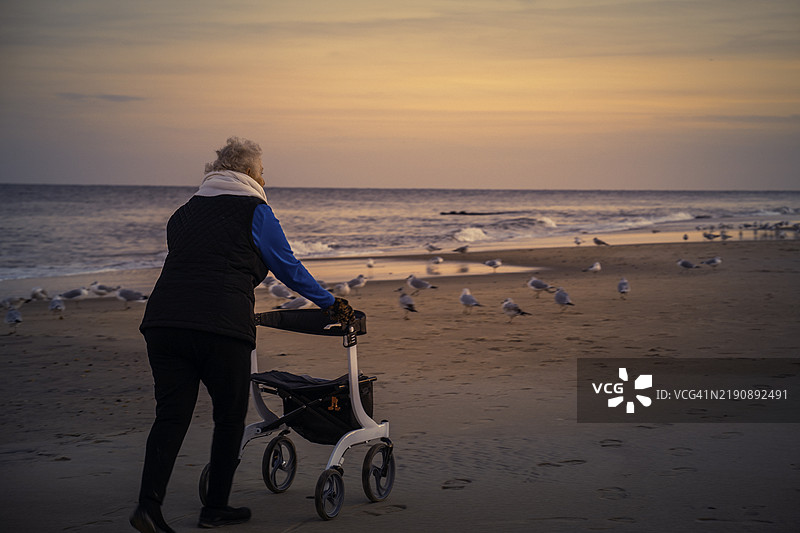 一位年长女性在日落时分使用助行器在雷霍博斯海滩上行走图片素材
