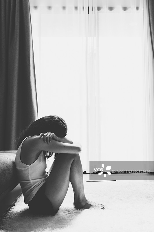黑白照片，抑郁的女人独自坐在客厅里。图片素材