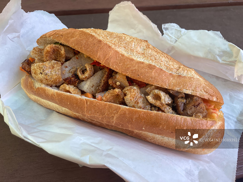 撕开的纸袋中装着烤猪肉和猪肉脆皮的越南法棍三明治，放在野餐桌上图片素材