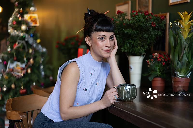 年轻女性在花店里享受热饮，感受圣诞气氛。图片素材
