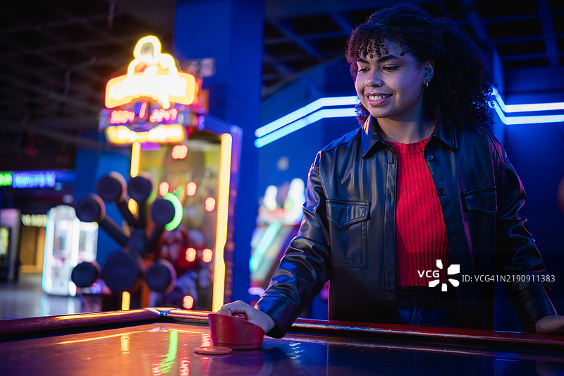 年轻女性在霓虹灯下的游戏厅里玩空气曲棍球图片素材