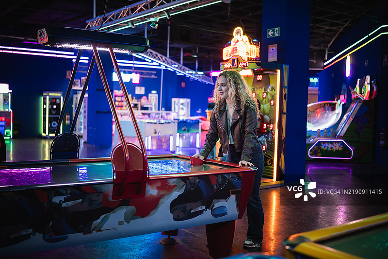 年轻女性在色彩缤纷的游戏厅里玩空气曲棍球图片素材