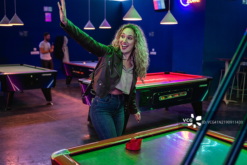 年轻女性在台球厅玩空气曲棍球并挥手致意图片素材