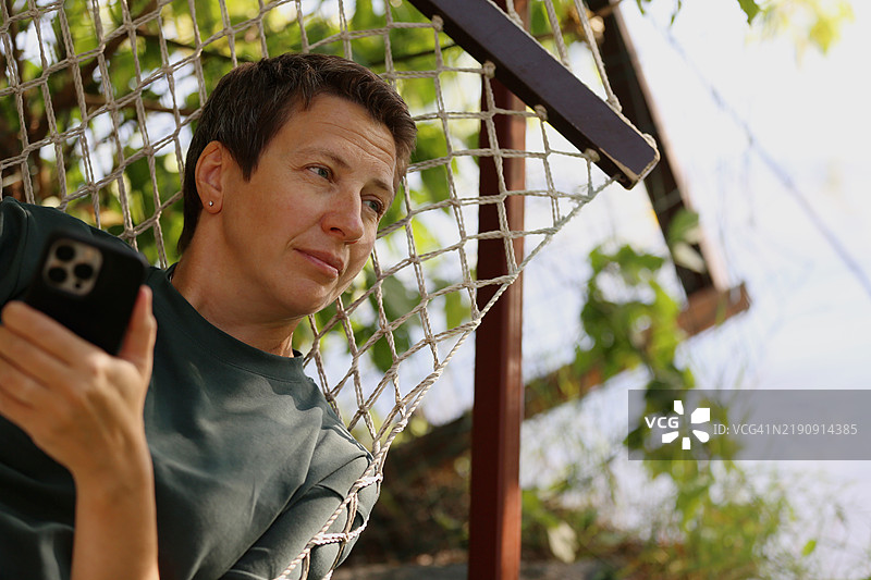 中年女性在森林中的吊床上使用手机放松图片素材