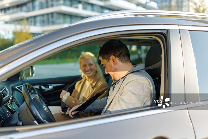 年轻情侣在车里系安全带，互相微笑。图片素材