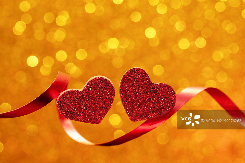 情人节庆祝活动，闪亮的红色心形和优雅的丝带，背景为温暖的金色。图片素材