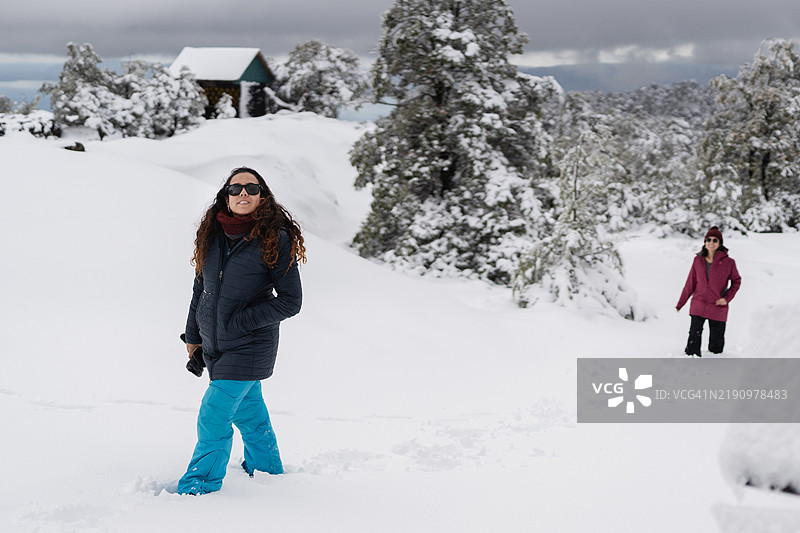 两名女性在雪山风景中徒步旅行，靠近一间小木屋图片素材