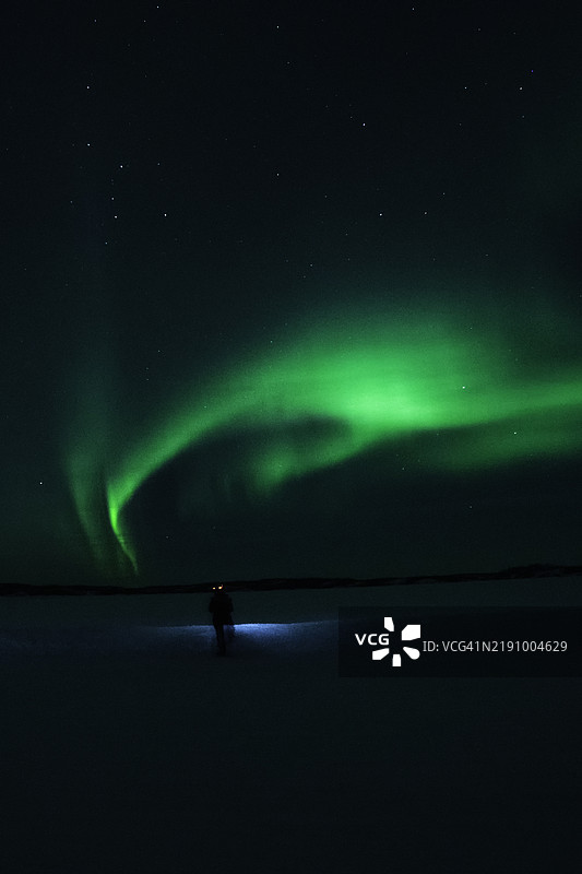 在加拿大西北地区黄刀镇，孤独地置身于旋转的北极光下图片素材