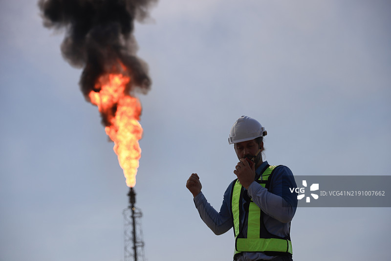 一位高级工程师在工厂熊熊大火的背景下使用对讲机。图片素材
