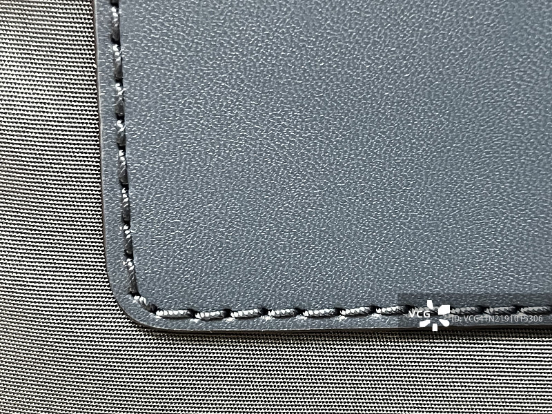 蓝灰色手提包的一部分，展示了纹理和缝线。图片素材