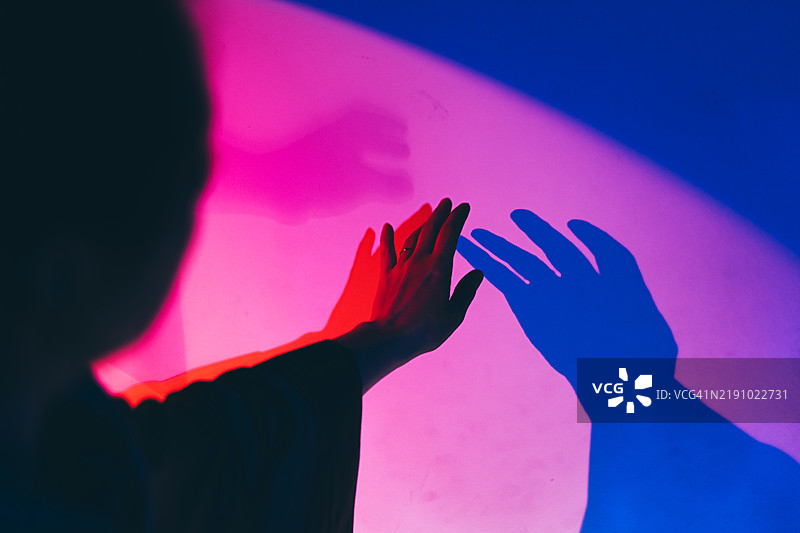 手投射出多彩的阴影：一侧是明亮的蓝色，另一侧是深红色。这个概念是二元性、连接以及光与影之间神秘的互动。图片素材