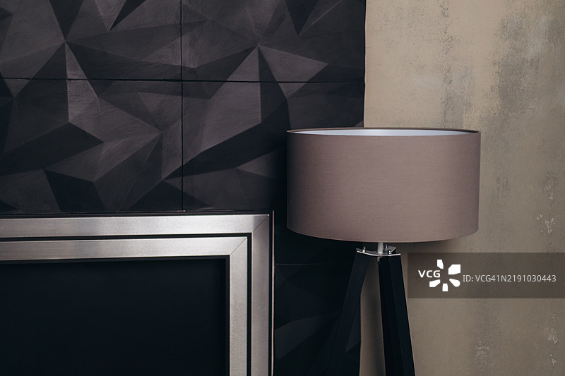 靠墙的圆柱形灯罩落地灯，墙面由深色多面砖和米色表面组成。图片素材
