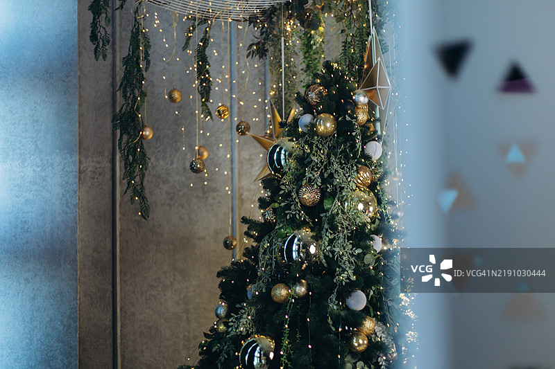 圣诞树，悬挂着金色球和星星，绿色植物映衬在有纹理的灰色墙壁上。图片素材