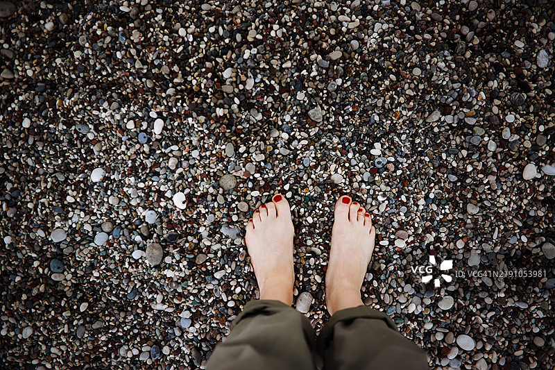 女人赤脚站在海滩的岩石上，俯视角度，放松和接地。图片素材