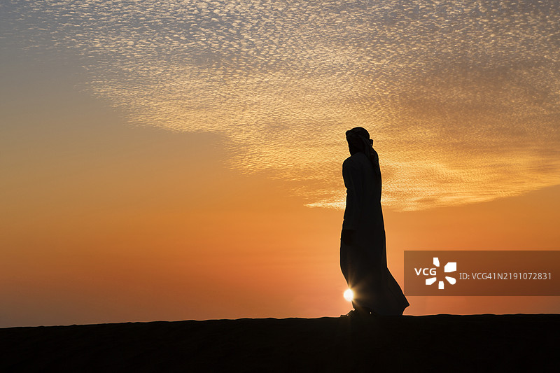 沙丘上日落时的阿拉伯男性剪影。图片素材