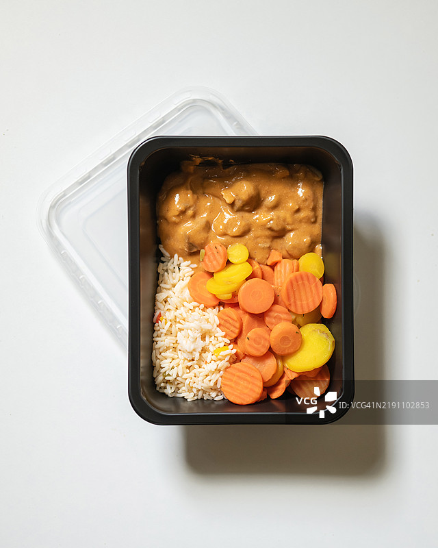塑料容器装有熟米饭、切片胡萝卜和奶油鸡肉炖菜。即食餐。微波炉加热。控制份量。快速消费。食品外送，外卖。商务午餐，晚餐。图片素材