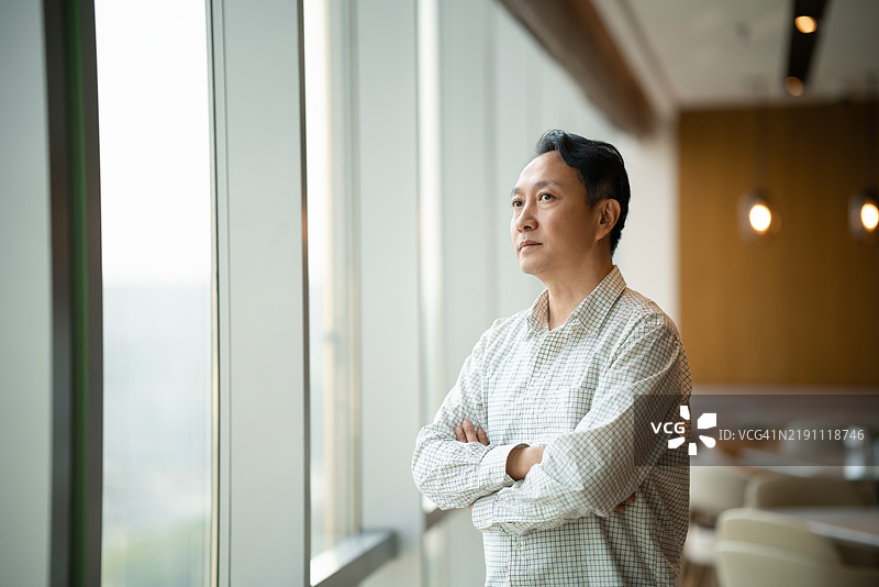 亚洲中年男子站在办公室的窗边图片素材