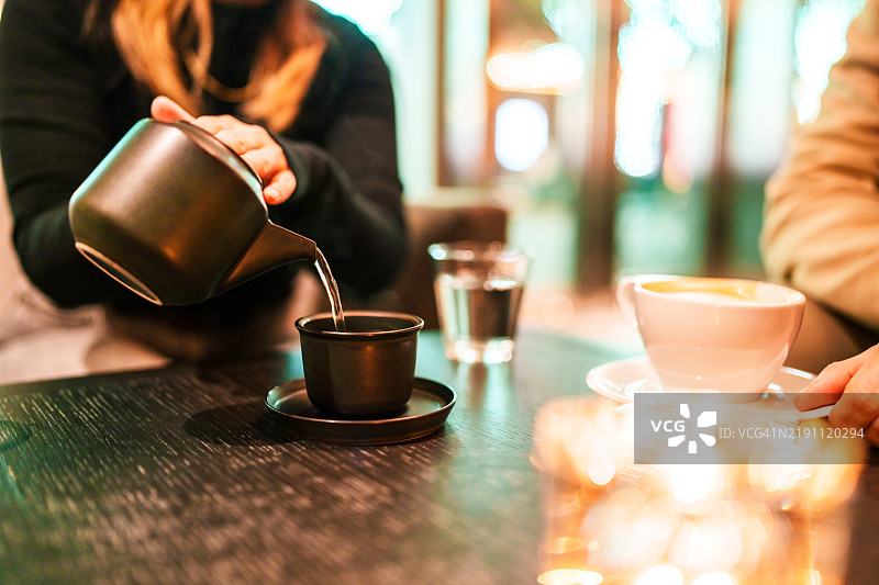 女人在杯子里倒热茶。图片素材