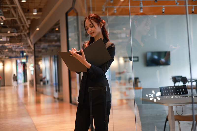 一位迷人的年轻亚洲女商人在现代办公室使用数字平板和智能手机应用进行工作，留有空白空间。图片素材