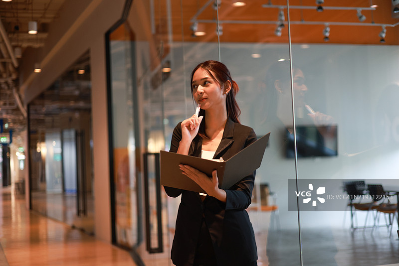 一位迷人的年轻亚洲女商人在现代办公室使用平板电脑和智能手机应用进行工作，留有空白空间。图片素材