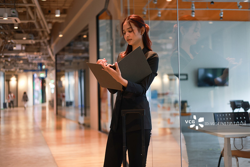 一位迷人的年轻亚洲女商人在现代办公室使用数字平板和智能手机应用进行工作，留有空白空间。图片素材