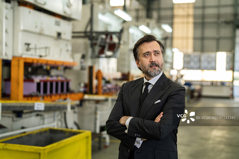 自信的商人在工业厂房环境中与机械设备合影图片素材