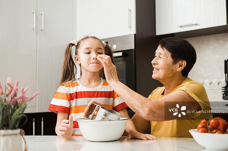 奶奶和 granddaughter 在厨房里一起做饭，鼻子沾满了面粉，玩得很开心。图片素材
