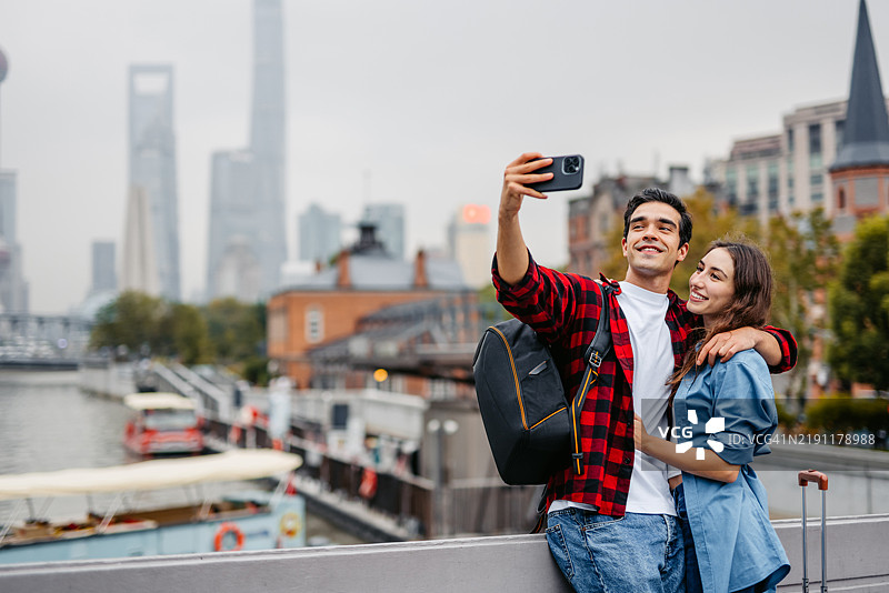 年轻情侣在中国上海的桥上用手机自拍图片素材