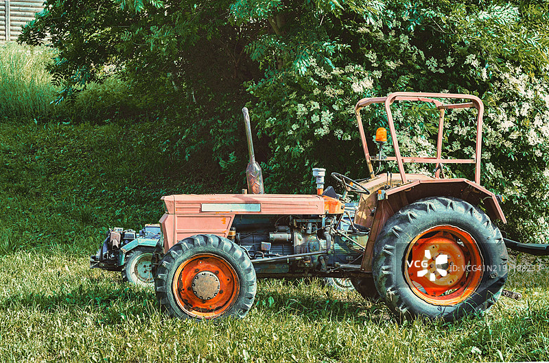 一张旧橙色拖拉机停在田野中的照片。照片拍摄于2024年6月，地点是意大利威尼托地区的圣斯特凡诺·迪·卡多雷镇。照片是在白天拍摄的。图片素材