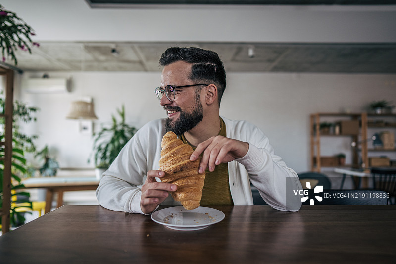 一个男人在早餐时吃可颂面包图片素材