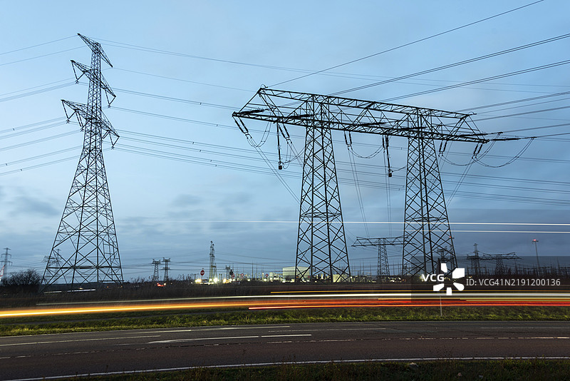 黄昏时分，德国萨克森-安哈尔特州沃尔米尔施泰特附近公路旁的高压电塔，路上留下了经过车辆的微弱光迹。图片素材