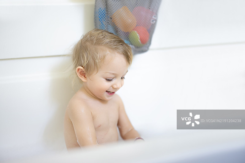 微笑的孩子在浴缸中享受玩耍时光，周围是玩具和柔和的灯光图片素材