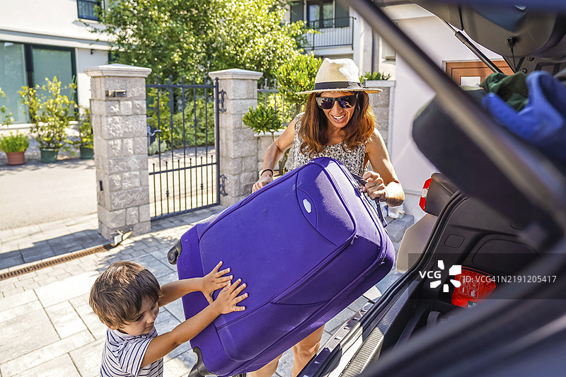 快乐的家庭，母亲和儿子正在把行李装进汽车后备箱，准备开始夏季公路旅行。图片素材