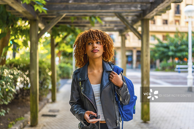 拉丁美女卷发，边走边用手机，背着背包在城市中行走图片素材