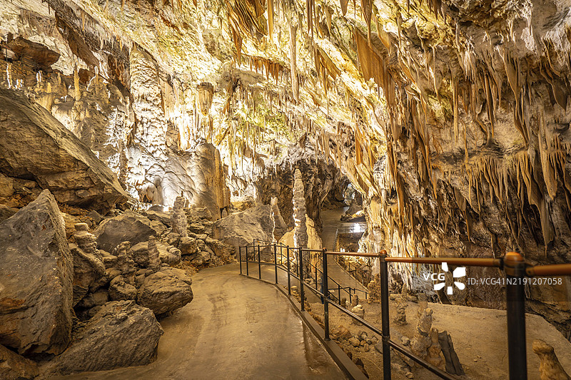 游客在斯洛文尼亚著名的波斯托伊纳洞穴参观，走在照明的水泥小径上，周围是钟乳石和石笋。图片素材