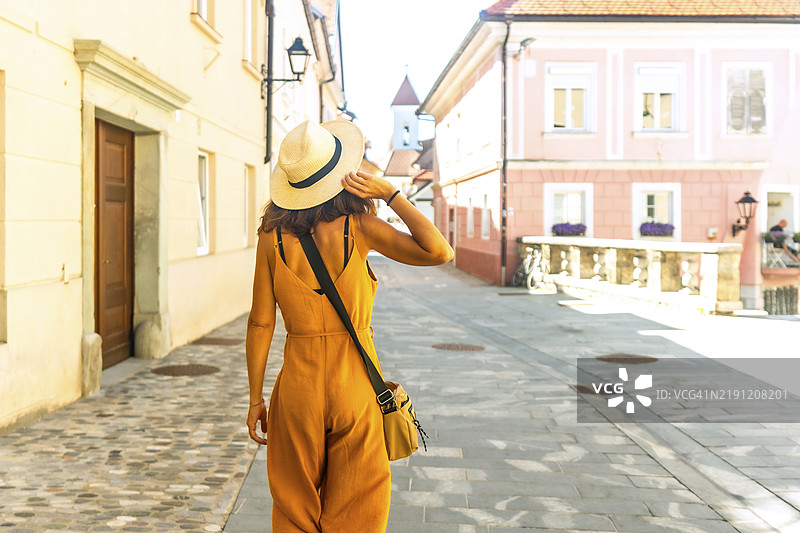 年轻女性游客戴着草帽，漫步在斯洛文尼亚克兰的风景如画的街道上，享受着欧洲的夏天和历史建筑。图片素材