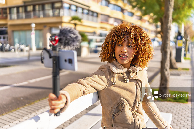 拉丁裔女性美丽的年轻博主在阳光明媚的秋天坐在城市楼梯上进行在线直播图片素材