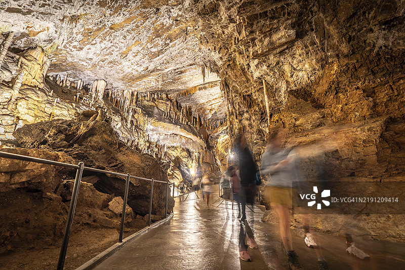 游客在斯洛文尼亚著名的波斯托伊纳洞穴内的混凝土人行道上行走，周围被人造灯光照亮。图片素材