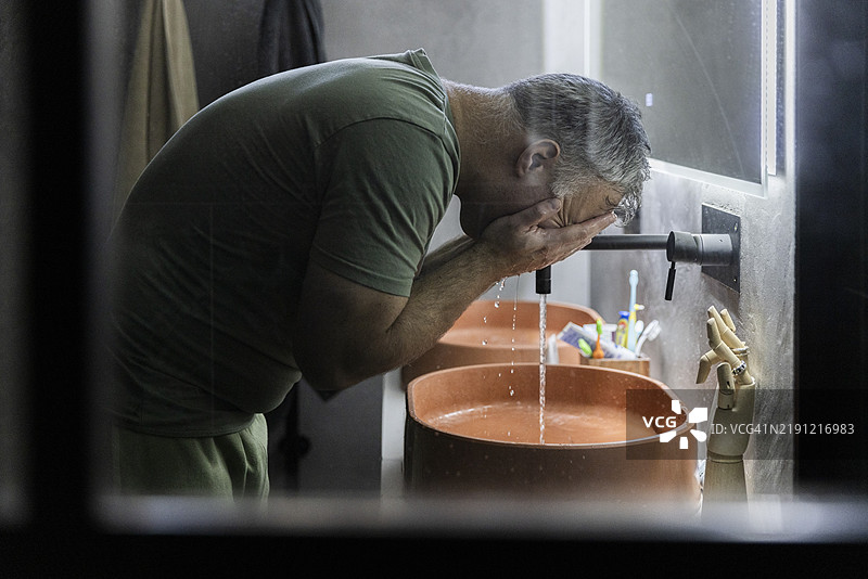 成熟男性在浴室洗手池侧面洗脸图片素材