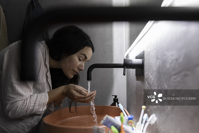 女人在浴室的水槽里用水洗脸图片素材