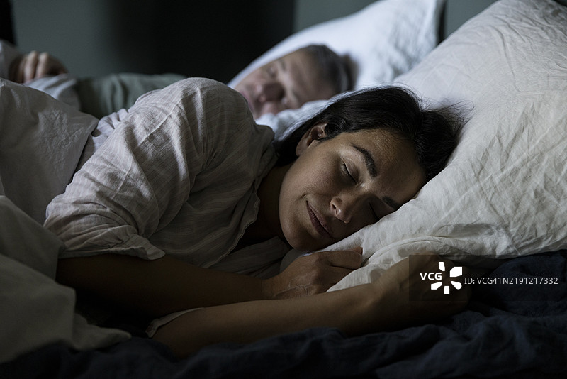 女人在家卧室的床上睡觉，旁边有一个男人。图片素材