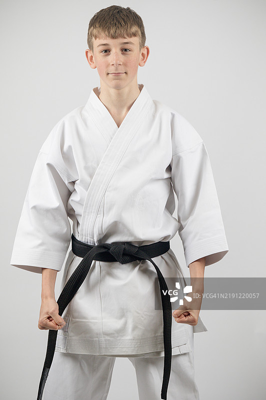 一名十五岁的少年，身穿黑带空手道服，背景为白色摄影棚。图片素材