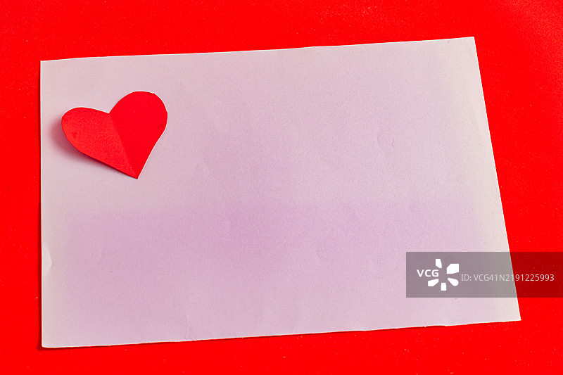 一张带有纸心的情书，放在紫色叶子上，背景是鲜艳的红色。图片素材