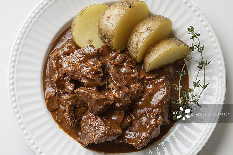 一张白色盘子上的煮土豆片和浓郁的棕色炖肉，炖肉中有大块牛肉。图片素材