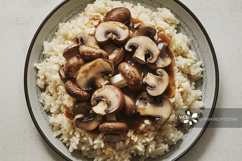 一只白色盘子里盛着奶油煮米饭，上面放着用丰富酱汁炒制的蘑菇。图片素材