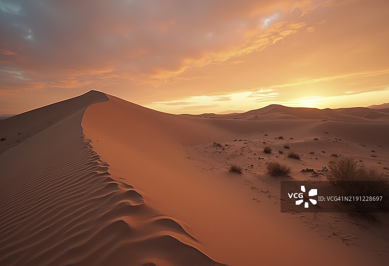 沙漠景观，沙丘与一条穿过沙地的路径，映衬在橙色的天空下图片素材