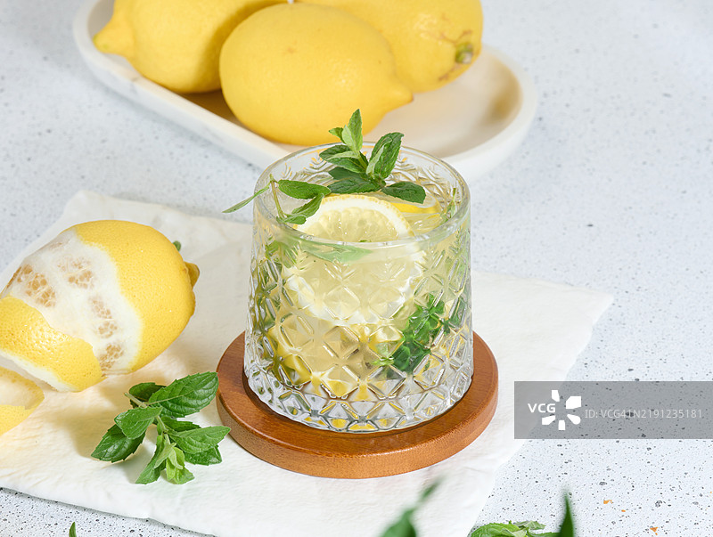 透明玻璃杯中放着柠檬片、薄荷叶和冰块，摆放在白色桌子上图片素材