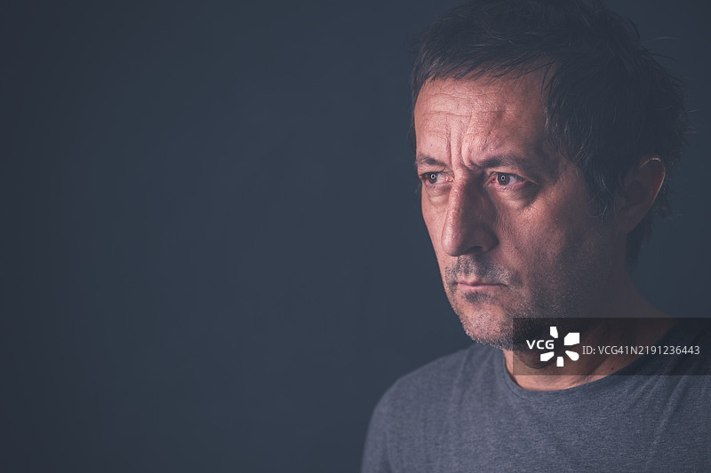 穿着灰色衬衫的中年男性在昏暗的房间里严肃地肖像照图片素材