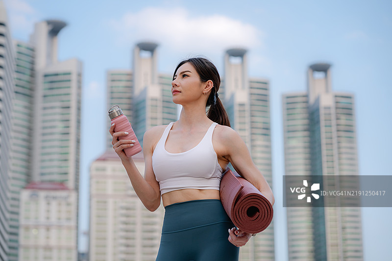 健康的亚洲女性手持瑜伽垫准备锻炼。都市生活方式概念。图片素材