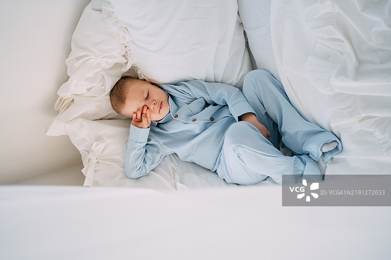 一个小男孩安静地躺在床上，穿着舒适的蓝色睡衣，享受着宁静的睡眠时光。图片素材